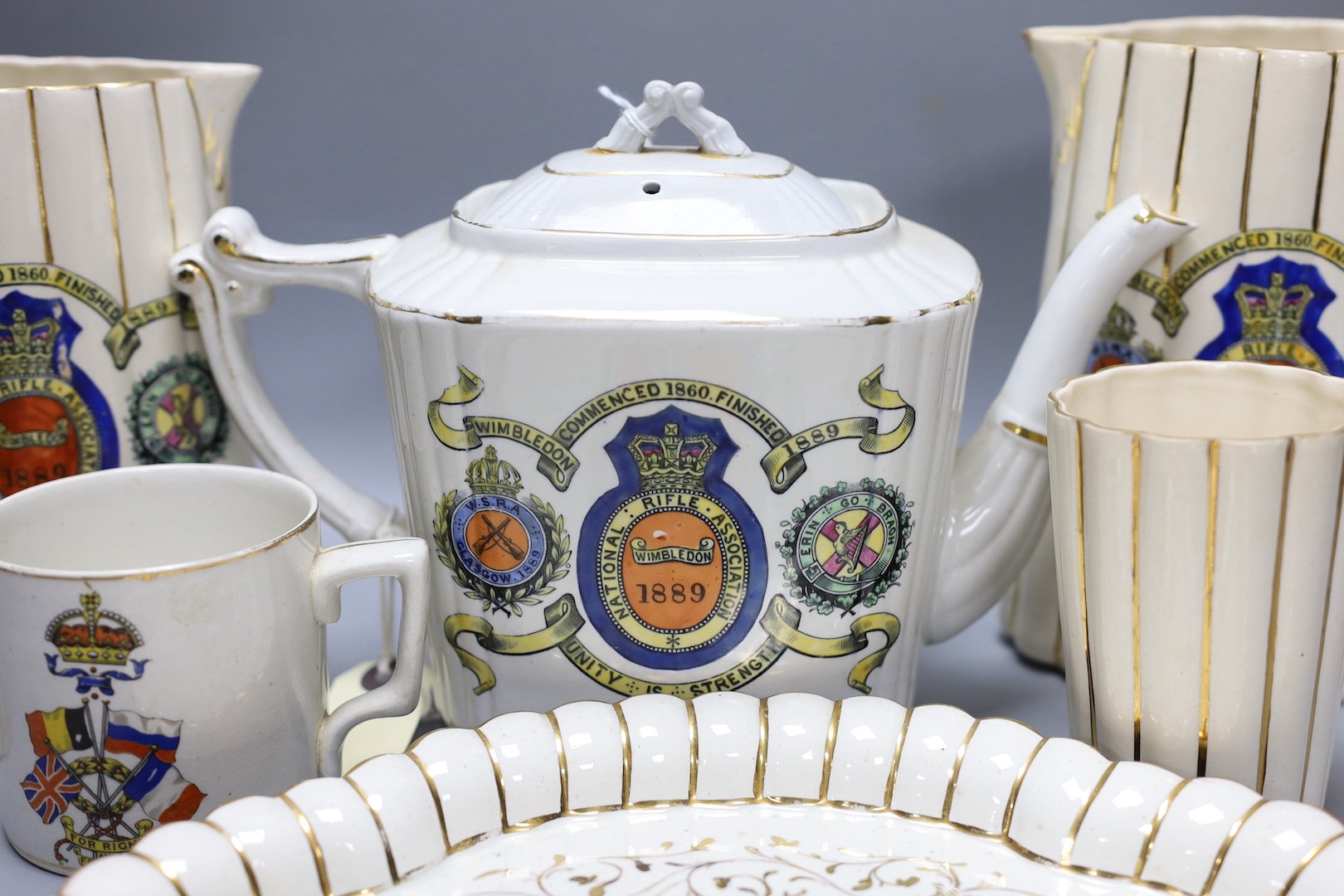 National Rifle Association Wimbledon 1889 - A group of Staffordshire commemorative pottery, including two water jugs, 18 cm high, and three matching beakers, a teapot and cover, a tray, together with a WW1 mug